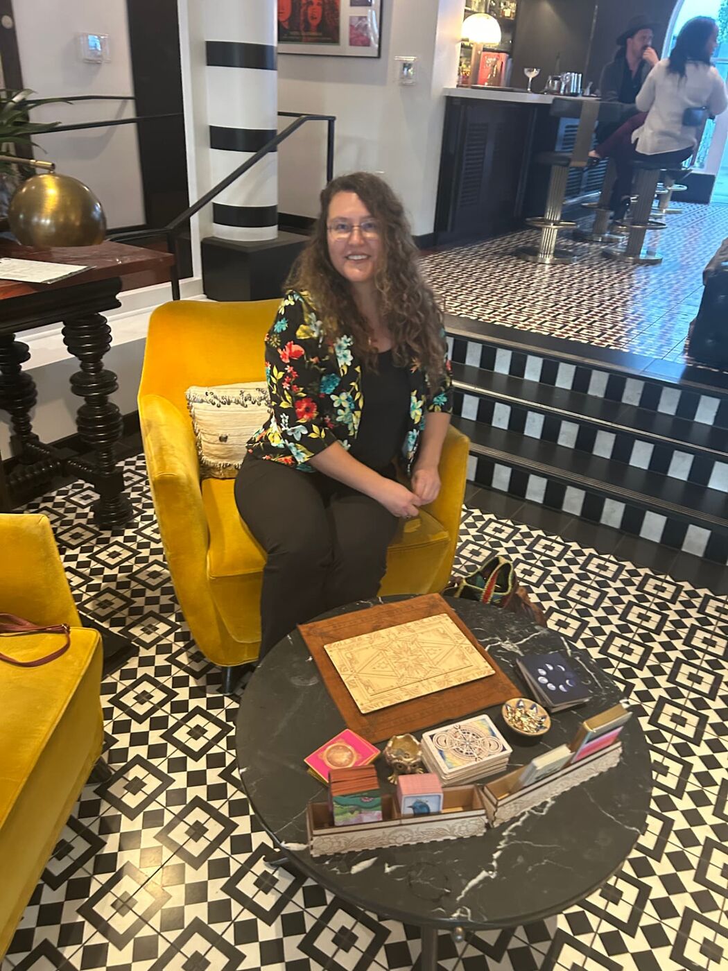 Mitra seated in a yellow armchair beside a reading table